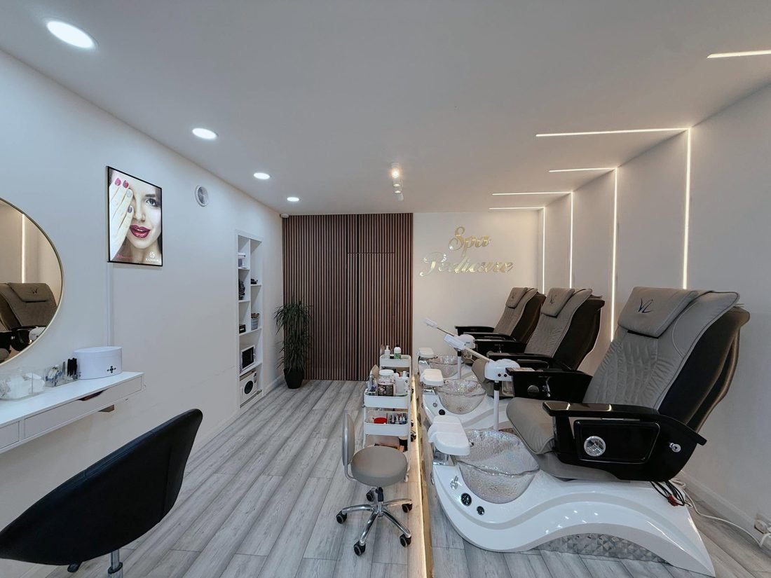 Pedicure chairs with basins along a bright wall inside the salon